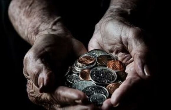 Older hands holding a handful of mixed coins against a dark background.