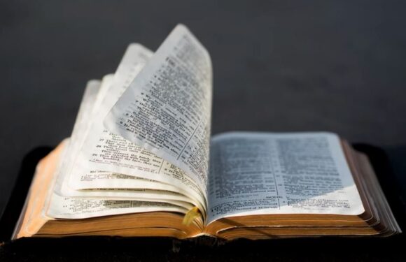 Open Bible with pages flipping, resting on a dark surface against a dark background.