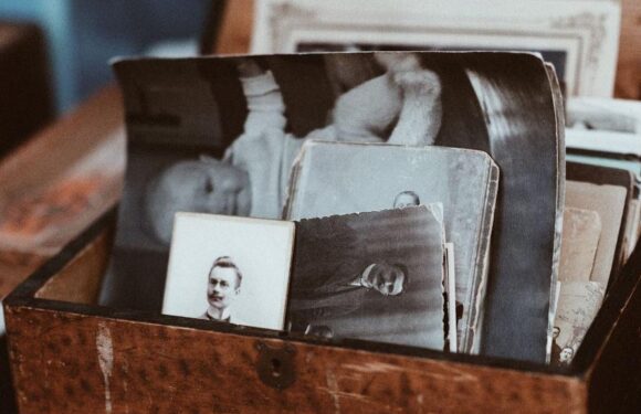 A wooden box containing black-and-white vintage photographs and postcards, with some images depicting people in formal attire and uniforms.