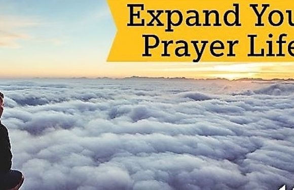 A person sitting on a mountain peak overlooking a sea of clouds at sunrise, with the text "Expand Your Prayer Life" in a yellow banner.