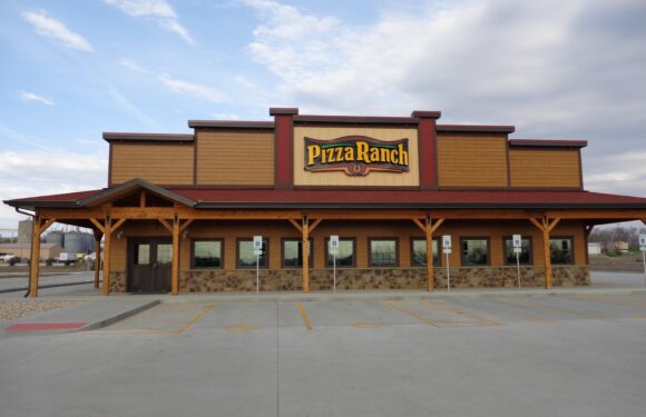 A large, modern restaurant with a wooden and stone exterior, and a prominent sign that reads "Pizza Ranch" above the entrance. The parking lot is mostly empty.