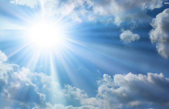 Bright sun shining through a partly cloudy sky with rays of sunlight and a few scattered clouds.