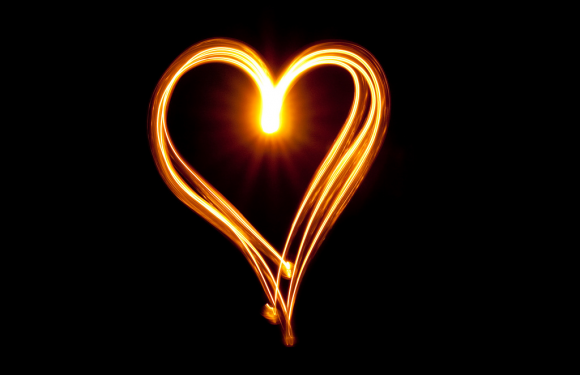 A glowing, fiery heart shape drawn with light trails against a black background.