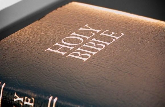 A close-up of a Bible with a textured brown cover, illuminated by a warm light, showing the title "HOLY BIBLE" embossed on the front.