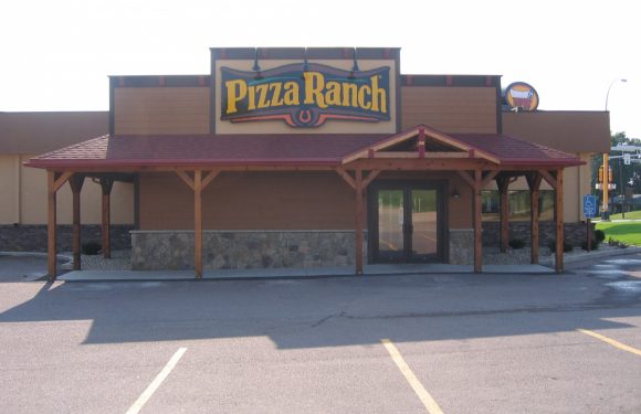 A Pizza Ranch restaurant with a wooden awning structure at the entrance, large sign on the facade, and surrounded by a parking lot.