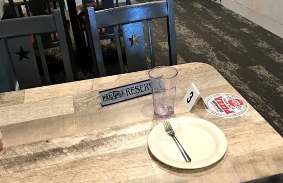 Empty table with a white plate, fork, purple plastic cup, and reservation sign. Several chairs with star cutouts in a casual restaurant setting.