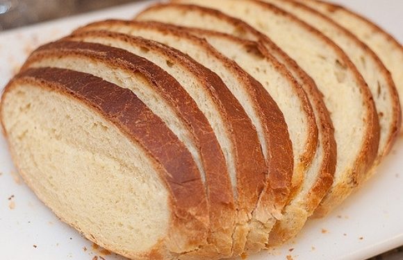 Sliced loaf of bread with a golden-brown crust and soft, white interior on a white plate.