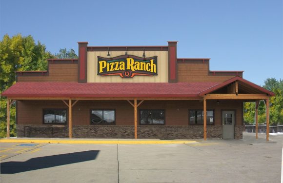 A single-story Pizza Ranch restaurant with a brick and wood exterior, large sign above the entrance, parking lot in front, and a clear blue sky.