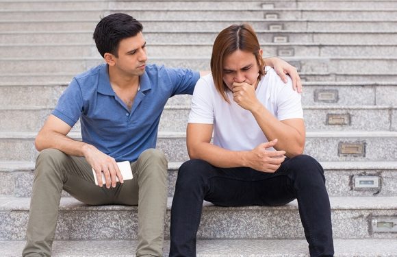 A young man comforts a distressed woman sitting on concrete steps, with both appearing to share an emotional moment.