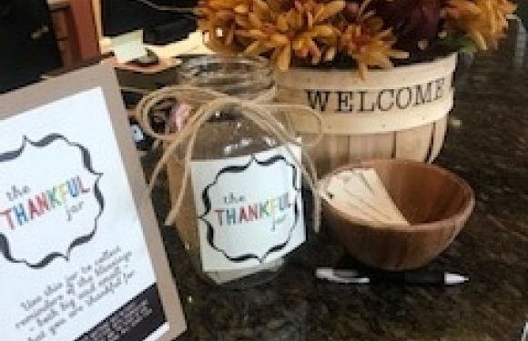 A welcoming floral arrangement with orange, yellow, and red flowers in a white "WELCOME" bowl, along with thank you signs and a small wooden bowl on a dark countertop.