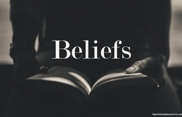 A person holding an open book with the word "Beliefs" overlaid in white text, in a monochrome setting.