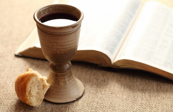 A wooden goblet filled with dark wine, a partially eaten biscuit, and an open book on a textured beige surface.