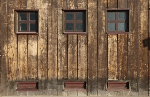 Wooden barn wall with three small, square windows near the top and three rectangular vents near the bottom, all framed in dark brown.