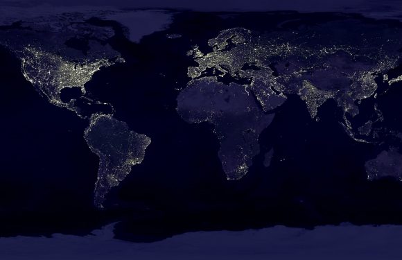A map of the world at night showing illuminated cities and regions, with dark oceans and landmasses, highlighting global light patterns.