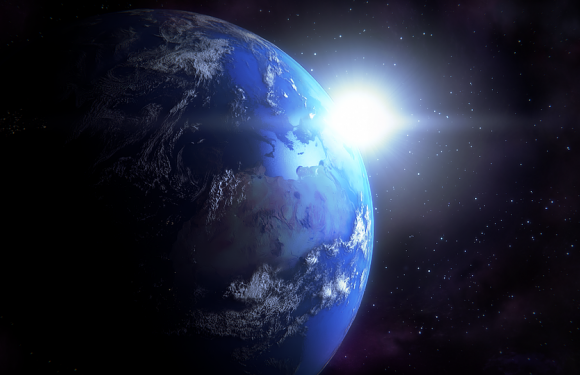 Earth seen from space with the sun shining in the background, surrounded by stars. The planet displays landmasses and water, with a glow from the sunlight.