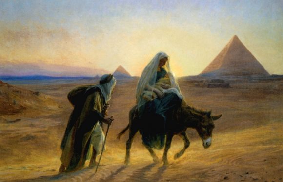A woman riding a donkey holding a baby, accompanied by a man walking beside her, with pyramids in the background at sunset.