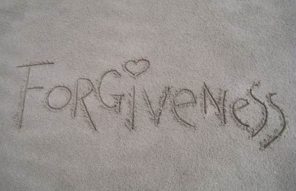 The word "Forgiveness" is written in the sand, with a small heart shape replacing the dot over the "i".