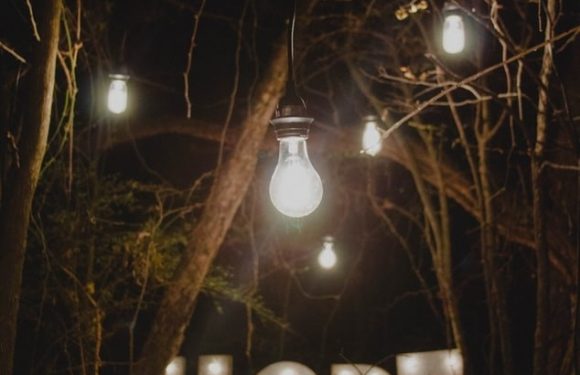 String lights hang above a wooded area spelling out "HOPE" with glowing letters on the ground, creating a warm, hopeful atmosphere at night.