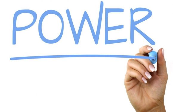 A hand holding a blue marker writing the word "POWER" in large blue letters on a white background.