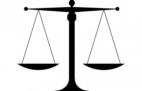 A black silhouettes of balanced scales symbolizing justice, with a central pole, horizontal bar, and two hanging pans.