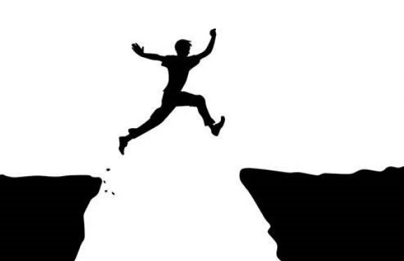 Silhouette of a person jumping across a gap between two cliffs.