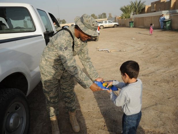 Army members giving crayons and coloring book to a little boy
