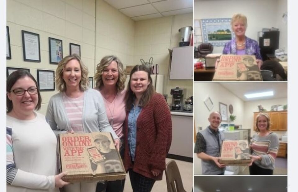 Group of five women and two men in a room, holding a pizza box with "Order & Online App" on it, smiling for a photo during Teacher Appreciation Day celebration.