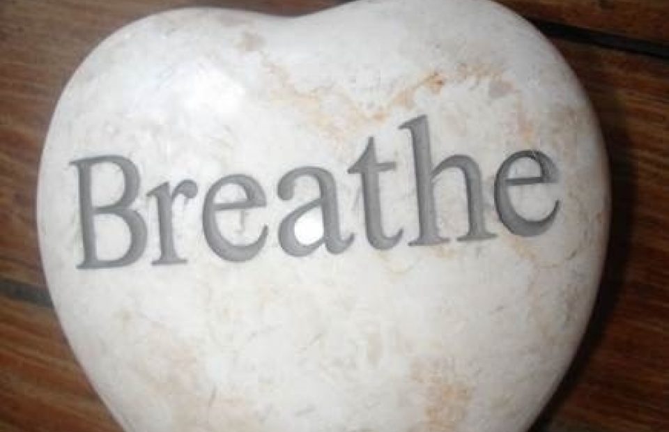 A heart-shaped stone with the word "Breathe" engraved on it, placed on a wooden surface.