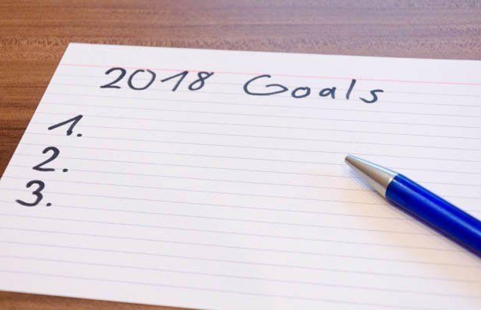 A handwritten list titled "2018 Goals" on lined paper with three numbered lines and a blue pen resting on the right side.