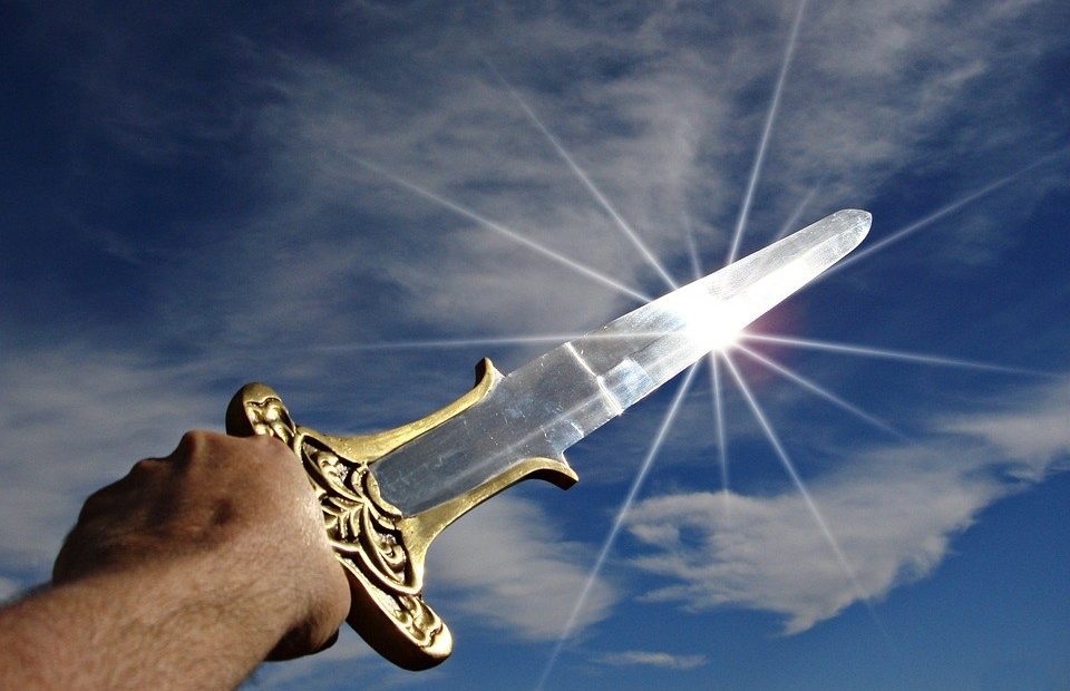 A hand holds a golden ornate dagger with a clear blade pointed towards the bright sun in a partly cloudy sky.